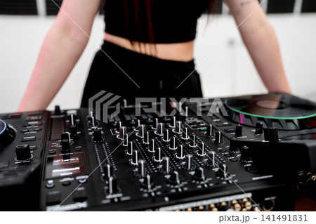 Close up of young woman artist DJ mixing and scratching music mixer controller. Attractive female musician DJ having fun mixing music on console touching buttons and playing electronic music Close up of young woman artist DJ mixing and scratching music mixer controller. Attractive female musician DJ having fun mixing music on console touching buttons and playing electronic music 141491831