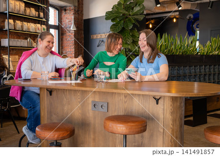 Colleagues or friends taking notes and collaborating at a stylish cafe counter in green setting. Collaboration, notes, cafe, counter, green. Colleagues or friends taking notes and collaborating at a stylish cafe counter in green setting. Collaboration, notes, cafe, counter, green. 141491857