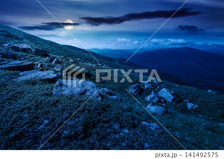 mountain landscape with grass and rock on a slope at night. mysterious view in to the distant valley of carpathian mountains. full moon over mountainous fantasy scenery of ukraine in summer mountain landscape with grass and rock on a slope at night. mysterious view in to the distant valley of carpathian mountains. full moon over mountainous fantasy scenery of ukraine in summer 141492575
