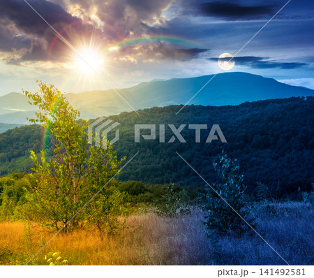 tree on a field in mountain landscape. day meet night. sun and moon over green countryside of ukraine in summer. cloudy weather. carpathian landscape in dappled light. amazing carpathian highland tree on a field in mountain landscape. day meet night. sun and moon over green countryside of ukraine in summer. cloudy weather. carpathian landscape in dappled light. amazing carpathian highland 141492581