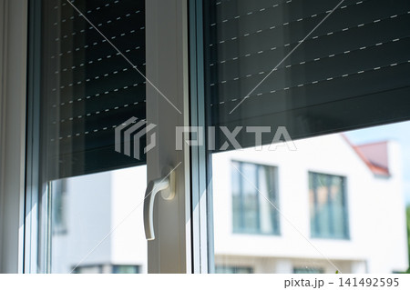 Roller shutters partially cover large windows with handle and neighboring house outside Roller shutters partially cover large windows with handle and neighboring house outside 141492595