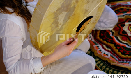 Close up of a practitioner playing a traditional frame drum, with natural skin texture filling the composition. Vibrational percussion supports meditation, relaxation, and inner balance. 141492720