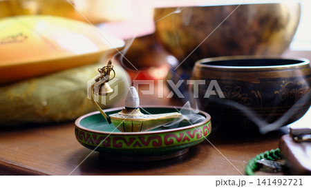Detailed close up of a smoldering incense cone in a decorative censer, with soft bokeh and bowls behind. Fragrance, meditation, and quiet evening rituals support comfort, self care, and relaxation. Detailed close up of a smoldering incense cone in a decorative censer, with soft bokeh and bowls behind. Fragrance, meditation, and quiet evening rituals support comfort, self care, and relaxation. 141492721