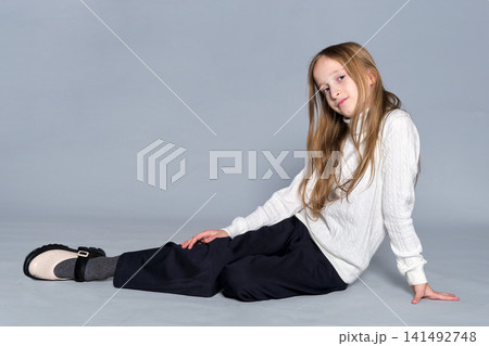 A young girl sits on the floor, stretching one arm out in a relaxed pose. A young girl sits on the floor, stretching one arm out in a relaxed pose. 141492748
