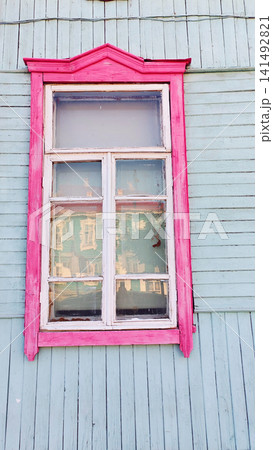 Vintage wooden house window with bright pink decorative frame on a pastel blue wall. The colorful architectural detail reflects traditional design, rural housing and charming historic building style. 141492821