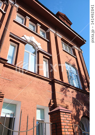 Close-up of a red brick facade with tall arched windows framed by white decorative keystones, showing signs of weathering and aging. Suitable for topics about facade restoration, historic masonry Close-up of a red brick facade with tall arched windows framed by white decorative keystones, showing signs of weathering and aging. Suitable for topics about facade restoration, historic masonry 141492841