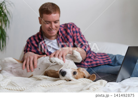 Delighted dog and owner sharing a tender moment, as man pauses from working on his laptop to give affection. Man taking a break from work on laptop Delighted dog and owner sharing a tender moment, as man pauses from working on his laptop to give affection. Man taking a break from work on laptop 141492875