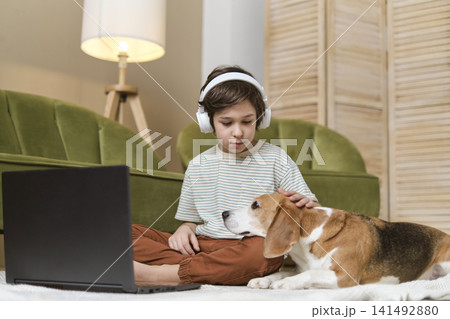 A little lad is seated on the living room floor during a virtual class, greeting his instructor as his Beagle buddy sits loyally beside him. Canine Companions in Digital Learning A little lad is seated on the living room floor during a virtual class, greeting his instructor as his Beagle buddy sits loyally beside him. Canine Companions in Digital Learning 141492880