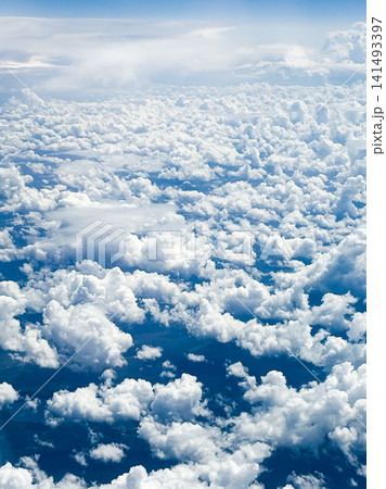 Many fluffy clouds scattered across blue sky during daylight top view from plane flying at high altitude. Clouds vary in size and shape, creating soft texture against vibrant blue background Many fluffy clouds scattered across blue sky during daylight top view from plane flying at high altitude. Clouds vary in size and shape, creating soft texture against vibrant blue background 141493397