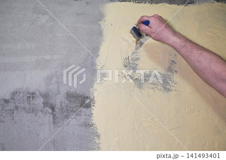 A hand of Person paints a wall yellow while waterproofing a bathroom under tiles. A hand of Person paints a wall yellow while waterproofing a bathroom under tiles. 141493401