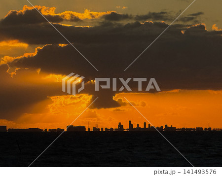 Golden clouds cast glow over city bay, serene ocean horizon captured during vibrant sunset moment Golden clouds cast glow over city bay, serene ocean horizon captured during vibrant sunset moment 141493576