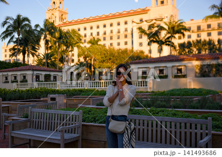 Woman In Sunglasses Standing In A Garden Near A Historic Hotel At Sunset Woman In Sunglasses Standing In A Garden Near A Historic Hotel At Sunset 141493686