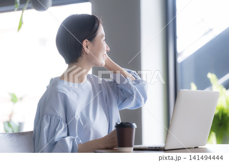ノートパソコンとコーヒーを前に窓の外を眺める日本人女性 オフィスで休憩する働く女性のイメージの横顔 141494444