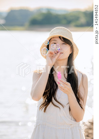 夏の水辺でシャボン玉を吹く麦わら帽子の女性 141494852
