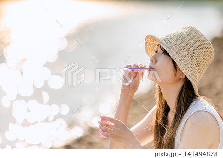 逆光にきらめくシャボン玉を吹く麦わら帽子の女性 逆光にきらめくシャボン玉を吹く麦わら帽子の女性 141494878