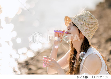 夏の光の中でシャボン玉を吹く麦わら帽子の女性 141494880