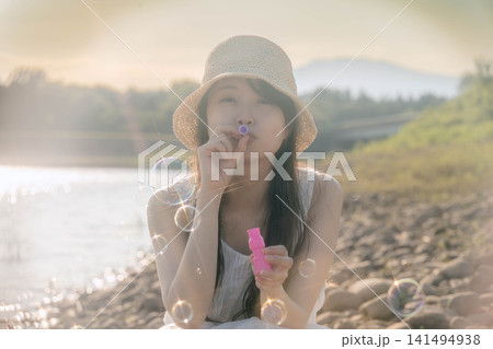 きらめく光の中でシャボン玉を飛ばす麦わら帽子の女性 きらめく光の中でシャボン玉を飛ばす麦わら帽子の女性 141494938