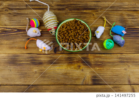 Set of toys for cat and bowl with dry pet food on wooden background. Top view. Pet care concept Set of toys for cat and bowl with dry pet food on wooden background. Top view. Pet care concept 141497255