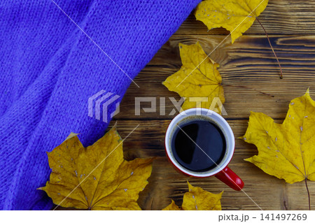 Cosy knitted blue sweater, cup of coffee and autumn maple leaves on wooden table. Top view. Autumn cozy concept Cosy knitted blue sweater, cup of coffee and autumn maple leaves on wooden table. Top view. Autumn cozy concept 141497269