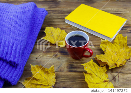 Cosy knitted blue sweater, book, cup of coffee and autumn maple leaves on wooden table. Autumn cozy concept 141497272