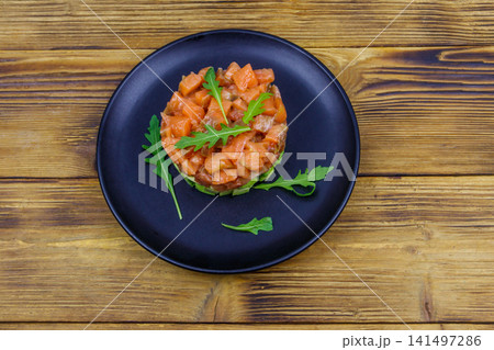 Salmon tartare with avocado and arugula on wooden table. Top view Salmon tartare with avocado and arugula on wooden table. Top view 141497286