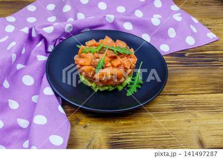 Salmon tartare with avocado and arugula on wooden table Salmon tartare with avocado and arugula on wooden table 141497287