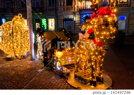 Illuminated Christmas deer with sleigh at night. Decoration for Christmas and New Years holidays in a city park Illuminated Christmas deer with sleigh at night. Decoration for Christmas and New Years holidays in a city park 141497296