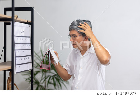 Senior Asian man with dementia struggles to set the time and day on his watch. Senior Asian man with dementia struggles to set the time and day on his watch. 141497977