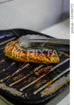 Grilled chicken breast cooking on pan with tongs, showing juicy texture and golden color, authentic home cooking and healthy protein meal concept 141498772