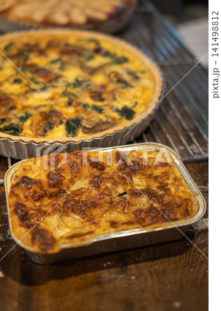 Fresh homemade lasagna with golden baked cheese and mushroom spinach quiche displayed on a rustic wooden table inside a bakery cafe 141498812