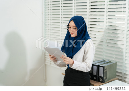 businesswoman reading information on report and laptop while writing a business plan in a modern office, strategy, productivity, planning, and corporate success. businesswoman reading information on report and laptop while writing a business plan in a modern office, strategy, productivity, planning, and corporate success. 141499281