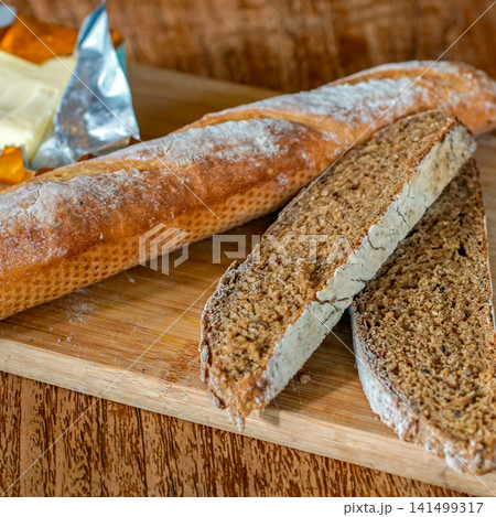 Fresh Artisan Baguette and Sliced Whole Grain Bread on Rustic Wooden Cutting Board with Natural Light Fresh Artisan Baguette and Sliced Whole Grain Bread on Rustic Wooden Cutting Board with Natural Light 141499317