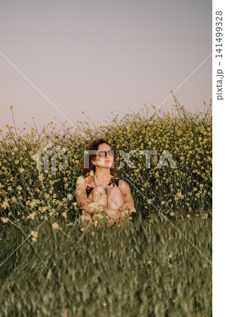 Woman flowers meadow sitting in a vibrant field of yellow mustard blossoms enjoying the peaceful spring sunshine during a quiet day Woman flowers meadow sitting in a vibrant field of yellow mustard blossoms enjoying the peaceful spring sunshine during a quiet day 141499328