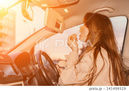 Woman car lipstick applying makeup while sitting in the driver seat during golden hour sunset Woman car lipstick applying makeup while sitting in the driver seat during golden hour sunset 141499329