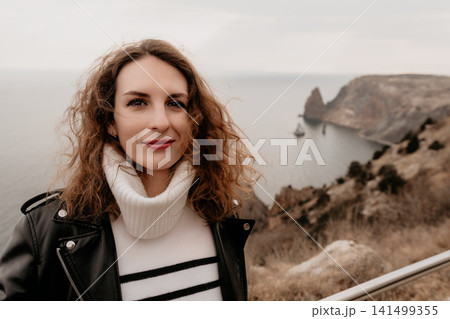 Woman leather portrait smiling on a rocky cliff overlooking the sea during an overcast day in autumn 141499355
