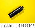 A dark bottle lies on a table against a yellow background. 141499407