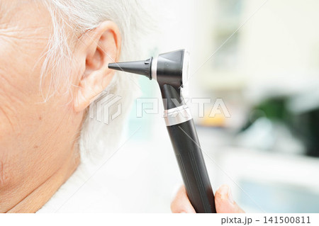 Otolaryngologist or ENT physician doctor examining senior patient ear with otoscope, hearing loss problem. 141500811