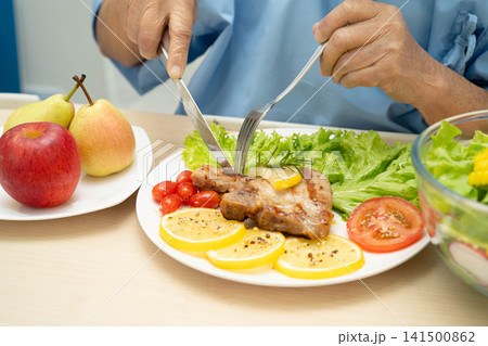 Asian elderly woman patient eating pork chop stake and vegetable salad for healthy food in hospital. Asian elderly woman patient eating pork chop stake and vegetable salad for healthy food in hospital. 141500862