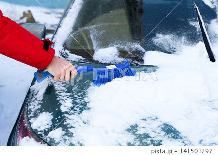 Hand using blue snow brush to clean car windshield in winter, close up view with copy space, cold weather vehicle maintenance concept. 141501297
