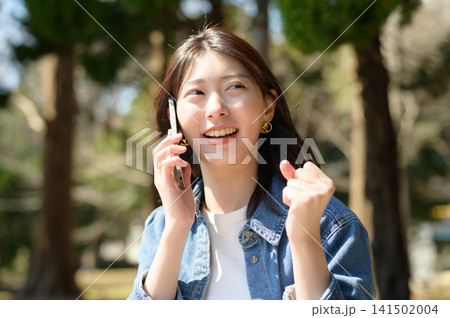 公園で電話しながらガッツポーズをする日本人女性 公園で電話しながらガッツポーズをする日本人女性 141502004