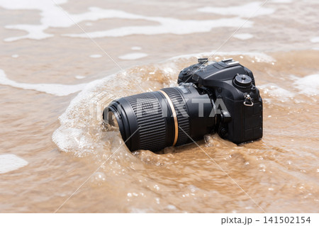 Professional camera partially submerged gentle ocean waves sandy beach illustrating water damage travel accident equipment risk Professional camera partially submerged gentle ocean waves sandy beach illustrating water damage travel accident equipment risk 141502154