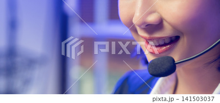 Smiling young Asian customer service representative wearing microphone headset and working on laptop 141503037