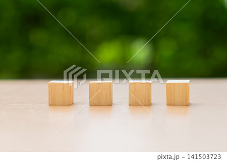 Four wooden blocks arranged in a straight line on table with green background. Four wooden blocks arranged in a straight line on table with green background. 141503723