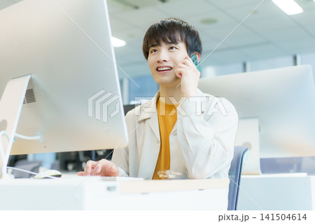 デスクトップパソコンで入力作業をしながらスマホで通話する若い日本人男性　 141504614