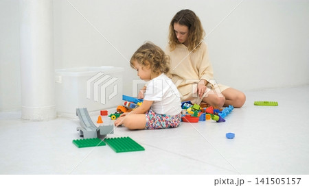 Sisters sitting together on the floor building structures with colorful plastic construction blocks. Family playtime concept Sisters sitting together on the floor building structures with colorful plastic construction blocks. Family playtime concept 141505157