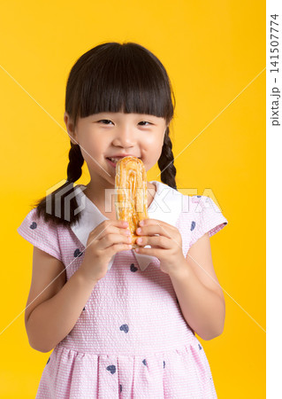 Cute Asian little girl eating sweet cookie, studio yellow background, happy smiling child enjoying dessert, childhood lifestyle concept Cute Asian little girl eating sweet cookie, studio yellow background, happy smiling child enjoying dessert, childhood lifestyle concept 141507774