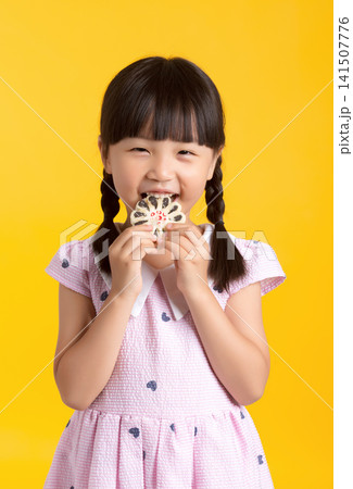 Cute Asian little girl eating sweet cookie, studio yellow background, happy smiling child enjoying dessert, childhood lifestyle concept Cute Asian little girl eating sweet cookie, studio yellow background, happy smiling child enjoying dessert, childhood lifestyle concept 141507776