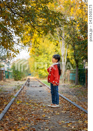 Adorable young girl strikes a cute pose on an empty train track surrounded by changing seasonal trees. 141508175