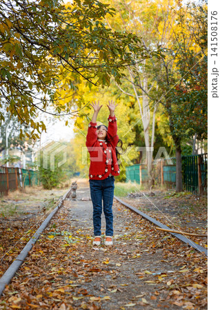 Adorable young girl strikes a cute pose on an empty train track surrounded by changing seasonal trees. 141508176