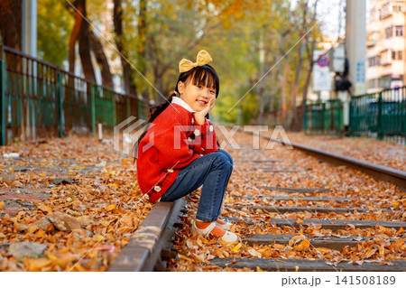 Little girl wearing a red sweater crouches on an old railway track ,On an autumn day 141508189